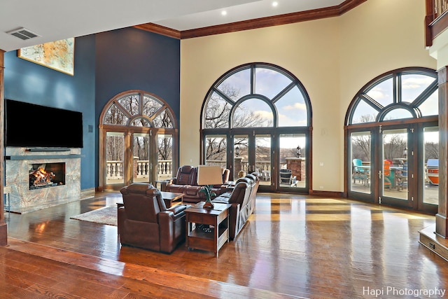 living room with a towering ceiling, hardwood / wood-style flooring, ornamental molding, a high end fireplace, and french doors