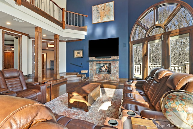 living room with crown molding, hardwood / wood-style floors, a towering ceiling, and ornate columns