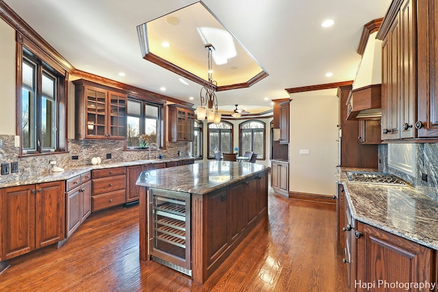 kitchen with dark stone countertops, wine cooler, ornamental molding, a kitchen island, and a raised ceiling