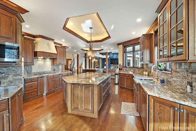 kitchen featuring sink, appliances with stainless steel finishes, a raised ceiling, custom range hood, and a kitchen island