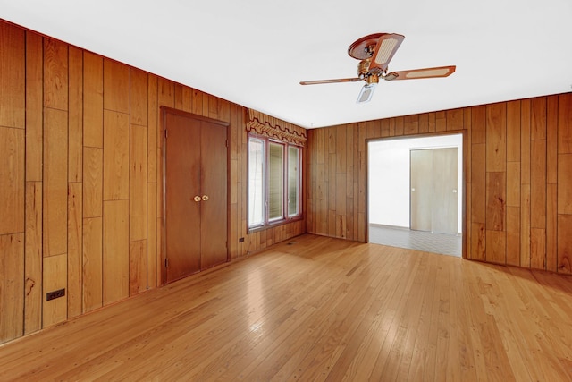 spare room featuring ceiling fan, wood walls, and light wood-type flooring