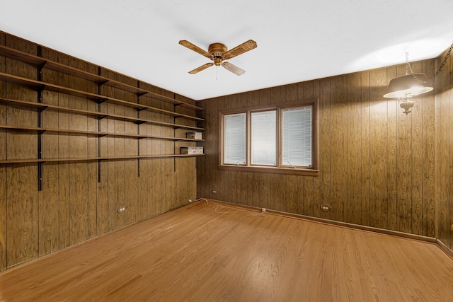 spare room with ceiling fan, wood walls, and light wood-type flooring