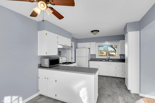 kitchen featuring sink, white appliances, white cabinetry, hardwood / wood-style floors, and kitchen peninsula