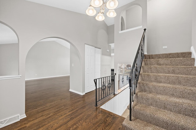 stairway with hardwood / wood-style floors, high vaulted ceiling, and a chandelier