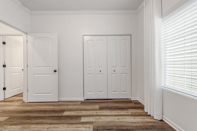 unfurnished bedroom with a closet, baseboards, crown molding, and light wood finished floors