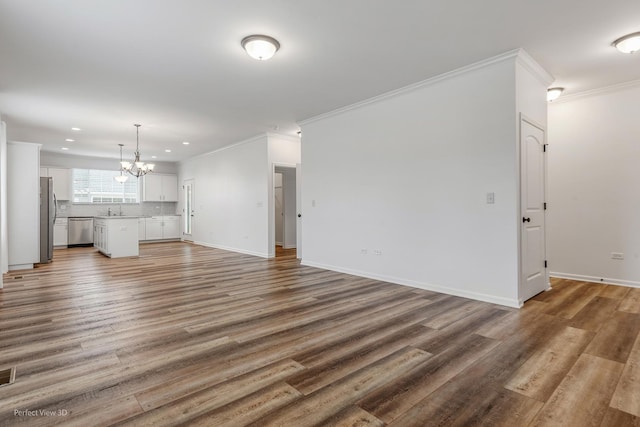 unfurnished living room with crown molding, a notable chandelier, baseboards, and wood finished floors