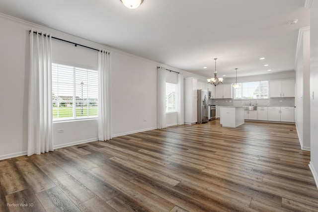 unfurnished living room with a healthy amount of sunlight, wood finished floors, and a notable chandelier