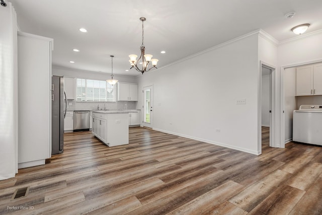 kitchen featuring decorative backsplash, appliances with stainless steel finishes, washer / clothes dryer, wood finished floors, and ornamental molding