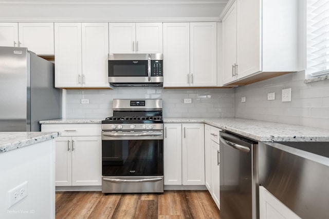 kitchen featuring light wood finished floors, white cabinets, appliances with stainless steel finishes, light stone countertops, and backsplash