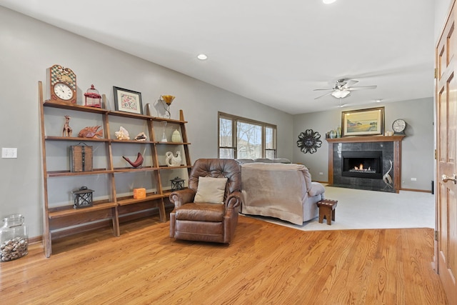 living area featuring ceiling fan, a tiled fireplace, and light wood-type flooring