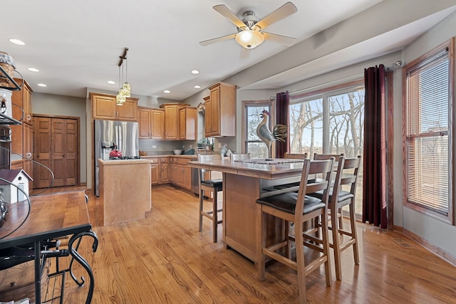 kitchen with a center island, a kitchen breakfast bar, stainless steel fridge, pendant lighting, and light hardwood / wood-style floors