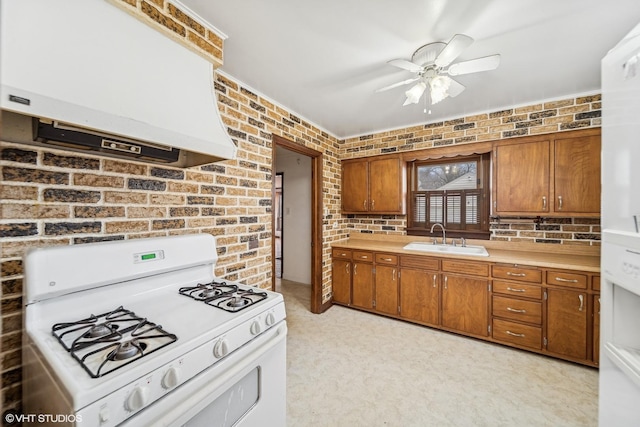 kitchen featuring sink, ceiling fan, custom range hood, brick wall, and white gas stove