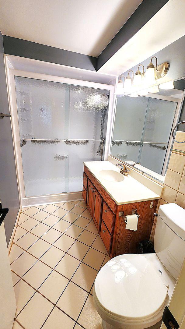 bathroom featuring walk in shower, vanity, toilet, and tile patterned flooring