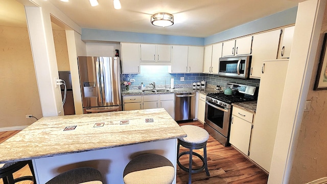 kitchen with white cabinetry, tasteful backsplash, wood-type flooring, stainless steel appliances, and light stone countertops