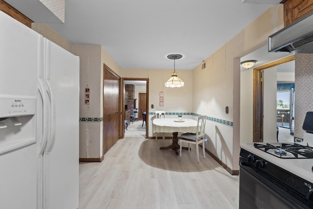 kitchen with range with gas stovetop, range hood, hanging light fixtures, white refrigerator with ice dispenser, and light hardwood / wood-style floors