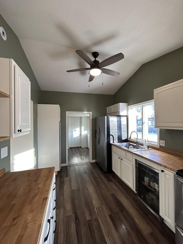 kitchen with butcher block counters, sink, white cabinetry, and vaulted ceiling