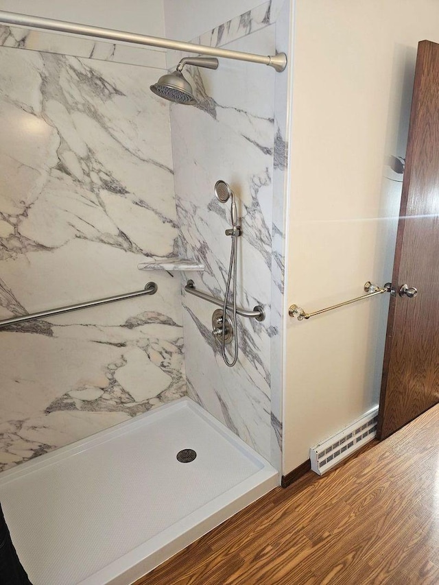 bathroom featuring baseboard heating, hardwood / wood-style floors, and a tile shower