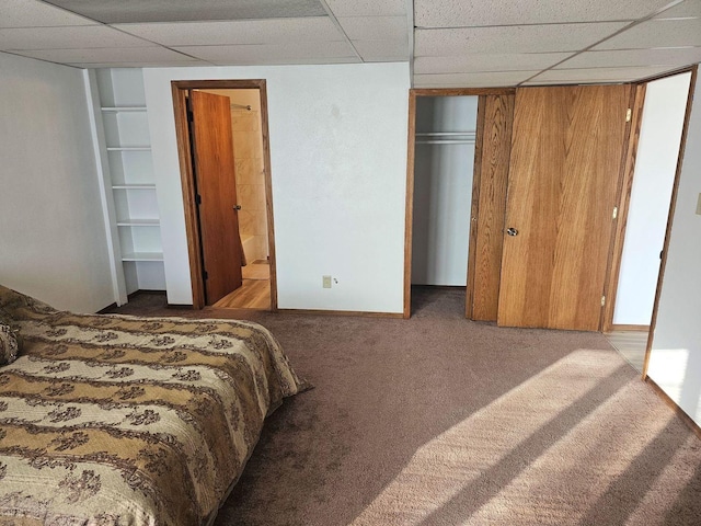 carpeted bedroom with connected bathroom and a drop ceiling