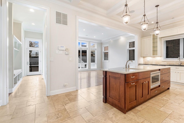 kitchen featuring sink, hanging light fixtures, a center island with sink, stainless steel microwave, and decorative backsplash