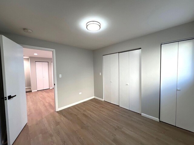 unfurnished bedroom with baseboards, two closets, and wood finished floors