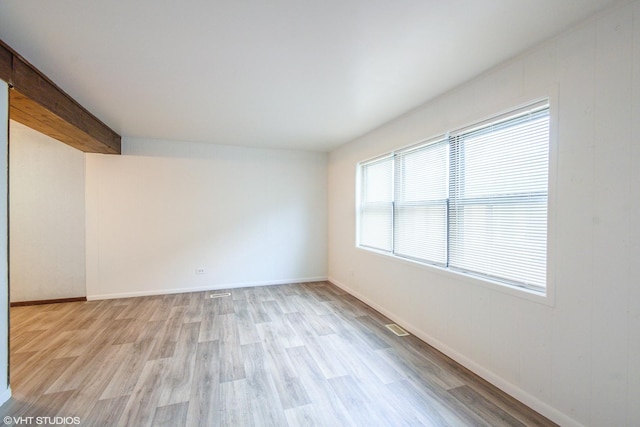 unfurnished room with beamed ceiling and light wood-type flooring