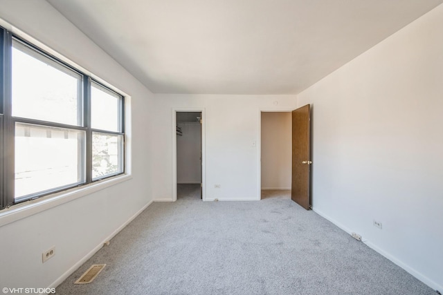 unfurnished bedroom with a walk in closet and light colored carpet