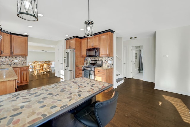 kitchen with tasteful backsplash, light stone counters, decorative light fixtures, appliances with stainless steel finishes, and dark hardwood / wood-style floors