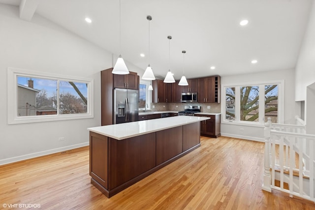 kitchen with a kitchen island, appliances with stainless steel finishes, pendant lighting, vaulted ceiling with beams, and light hardwood / wood-style floors