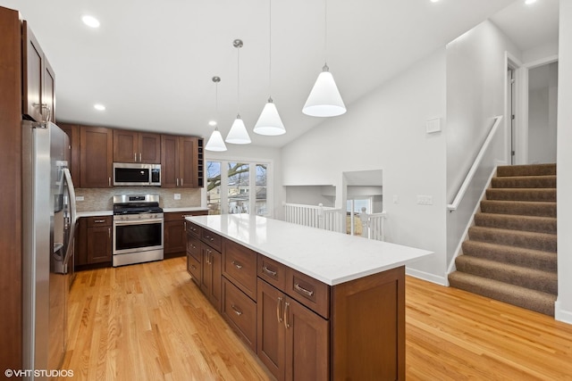 kitchen featuring pendant lighting, light hardwood / wood-style flooring, appliances with stainless steel finishes, a center island, and vaulted ceiling