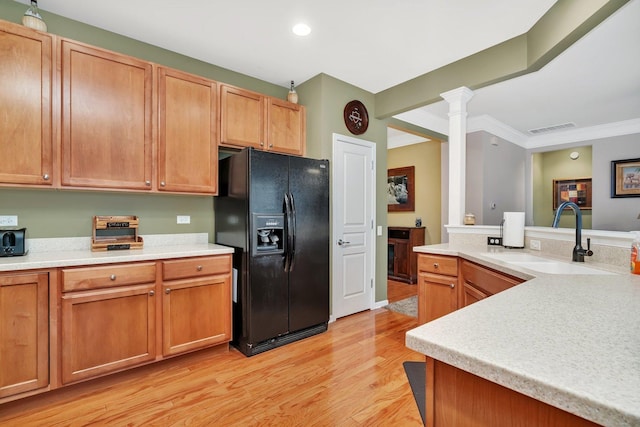 kitchen with sink, decorative columns, crown molding, black refrigerator with ice dispenser, and light hardwood / wood-style floors