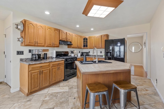 kitchen with sink, a breakfast bar, black appliances, an island with sink, and tile countertops