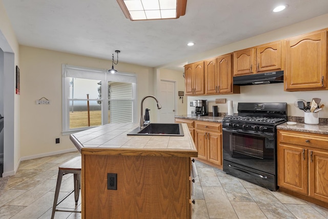 kitchen featuring sink, tile countertops, decorative light fixtures, a center island with sink, and black gas stove