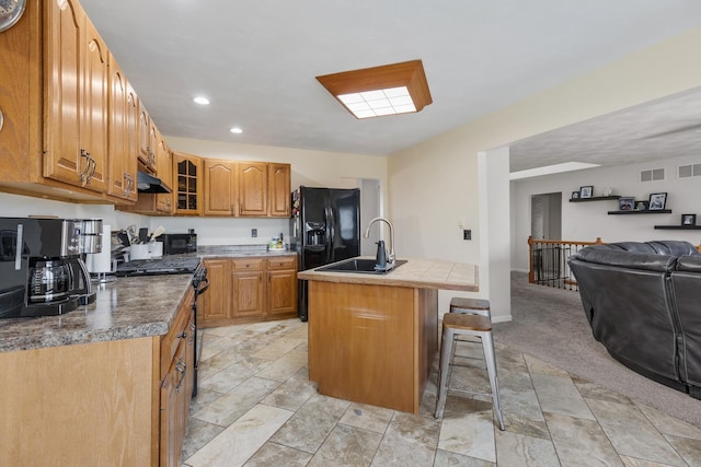 kitchen with a breakfast bar, sink, a kitchen island with sink, light colored carpet, and black appliances