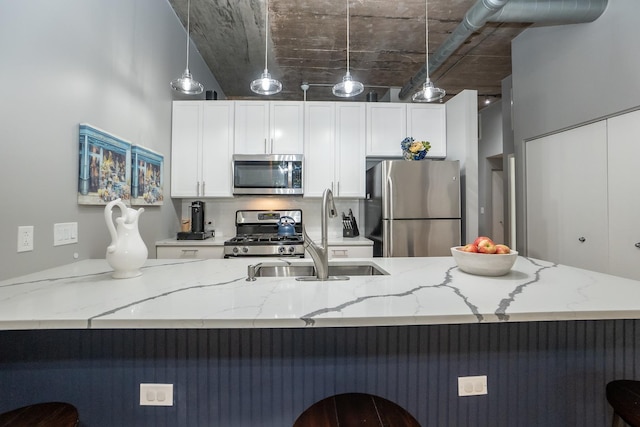 kitchen featuring white cabinets, a breakfast bar area, appliances with stainless steel finishes, hanging light fixtures, and a sink