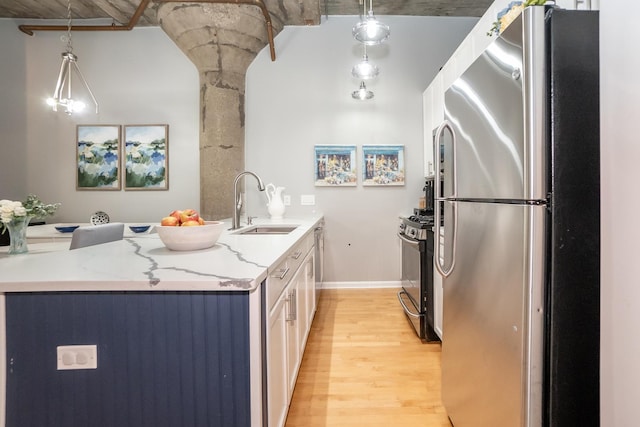 kitchen featuring light stone counters, a sink, hanging light fixtures, freestanding refrigerator, and gas stove