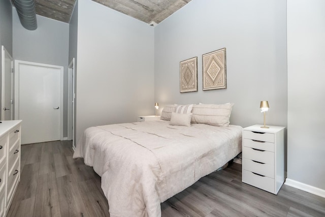 bedroom featuring dark wood finished floors, a towering ceiling, and baseboards