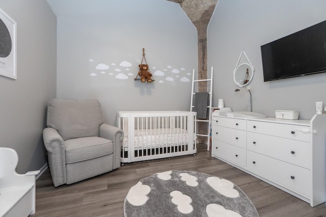 bedroom featuring a nursery area, arched walkways, and wood finished floors