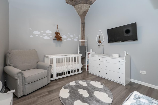 bedroom with a crib, baseboards, and wood finished floors