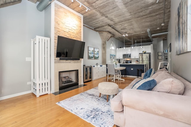 living area with a towering ceiling, track lighting, light wood-type flooring, baseboards, and a tile fireplace