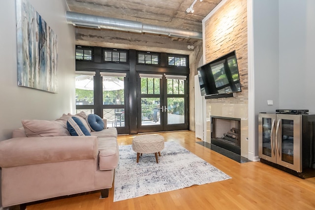 living room with wine cooler, a high ceiling, a fireplace, wood finished floors, and french doors