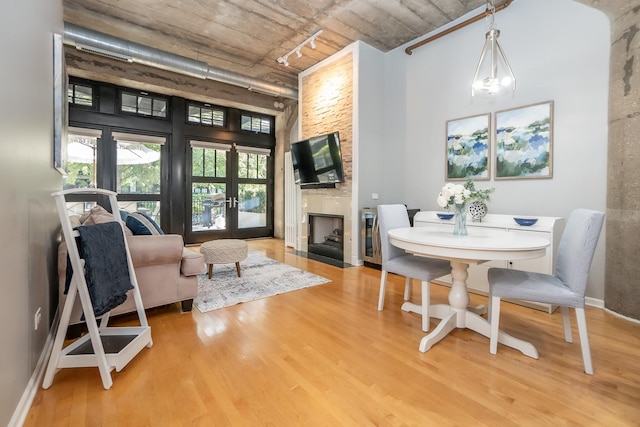 dining space featuring a fireplace, wood finished floors, a towering ceiling, french doors, and rail lighting