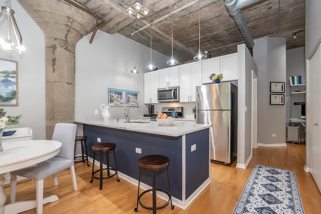 kitchen featuring a peninsula, stainless steel appliances, light countertops, a kitchen bar, and pendant lighting