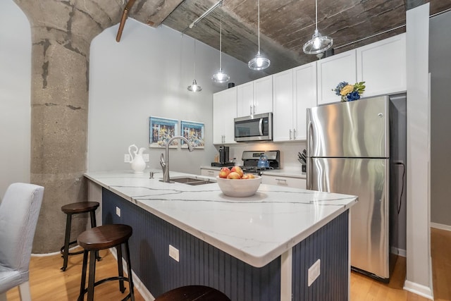 kitchen with a breakfast bar area, a sink, white cabinets, appliances with stainless steel finishes, and light stone countertops