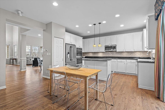 kitchen with pendant lighting, sink, appliances with stainless steel finishes, white cabinetry, and light hardwood / wood-style floors