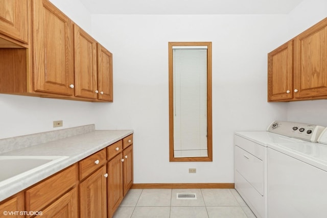 clothes washing area with washer and dryer, light tile patterned floors, and cabinets