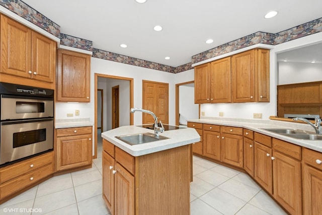 kitchen with an island with sink, sink, light tile patterned floors, and double oven