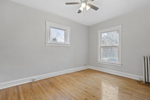 empty room featuring plenty of natural light, radiator heating unit, and light hardwood / wood-style flooring