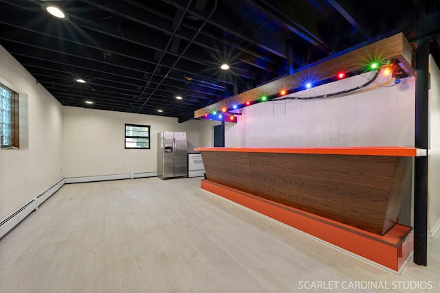 interior space with a baseboard heating unit, hardwood / wood-style flooring, stainless steel fridge, and indoor bar