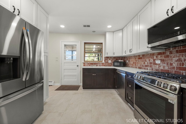 kitchen featuring sink, a baseboard heating unit, stainless steel appliances, white cabinets, and decorative backsplash