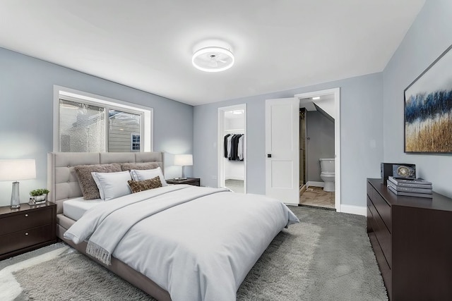 carpeted bedroom featuring baseboards, a closet, ensuite bathroom, and a walk in closet